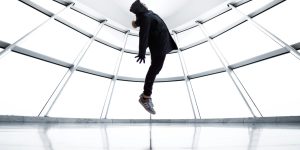 A person seemingly levitates in a contemporary room with reflections and shadows.