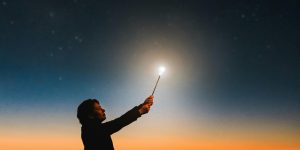 A silhouette of a person holding a glowing wand under a vibrant sunset sky, creating a magical atmosphere.